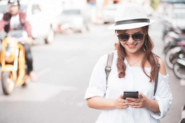 De Aziatische vrouwentoerist controleert het texting van smartphone op straat, gebruikend mobiele telefoonapp om kaart online te controleren.