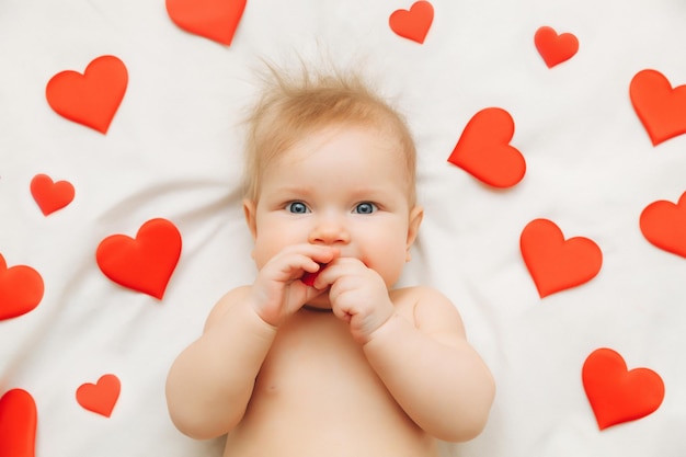 De baby is 6 maanden oud en ligt op het bed tussen harten het concept van liefde en Valentijnsdag