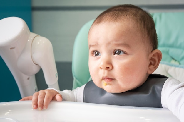 De baby is stout aan de tafel op de kinderstoel Hongerig overstuur kind weigert te eten introductie van aanvullend voedsel