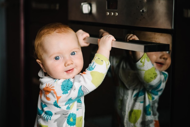 De baby leert staan in de buurt van de oven in de keuken Kleine negen maanden babyjongen staat met steun thuis Peuter heeft net geleerd hoe hij op haar voeten moet staan Close-up