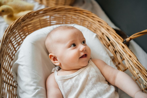 De baby ligt in een wicker mand met een grijze achtergrond in wilgen-eco-stijl.