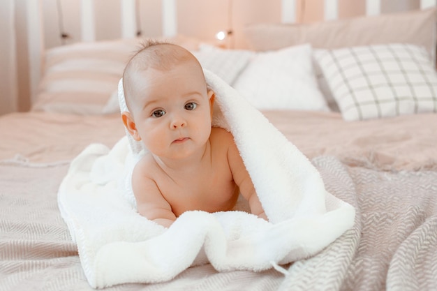 De baby ligt thuis bedekt met een handdoek op het bed na het baden