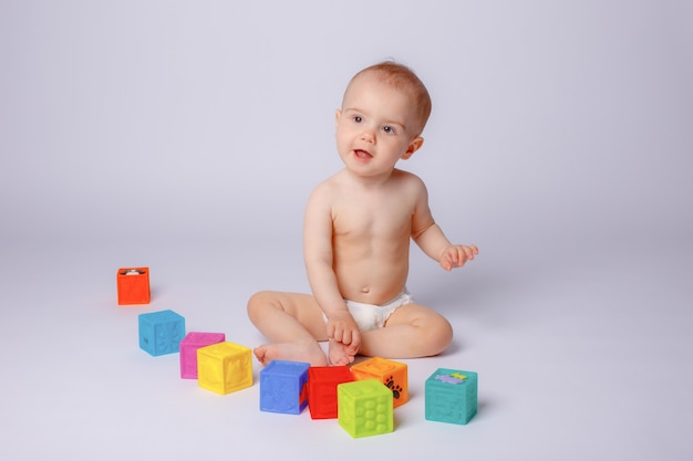 De baby speelt met kleurrijke blokjes in een luier op een witte achtergrond