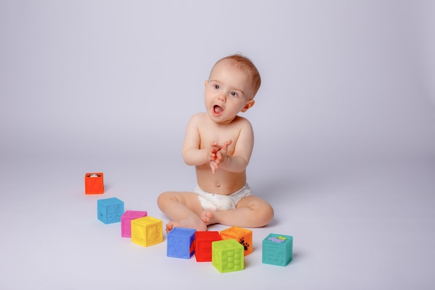 De baby speelt met kleurrijke blokjes in een luier op een witte achtergrond