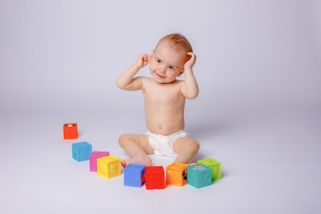 De baby speelt met kleurrijke blokjes in een luier op een witte achtergrond