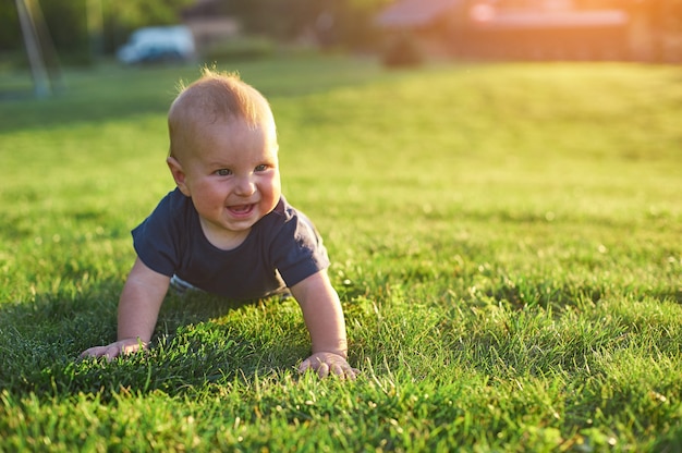 De babyjongen kruipt op een groen gazon in ochtendzonlicht.