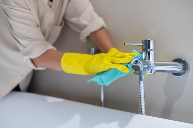 De badkamer schoonmaken. Een servicevrouw die de kraan in de badkamer polijst