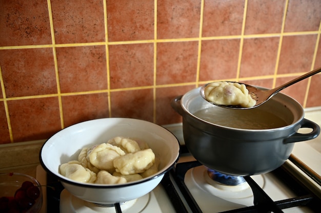 De banketbakker haalt gekookte dumplings uit kokend water in een vergiet. proces van het koken van dumplings stap voor stap. close-up, voedselachtergrond.