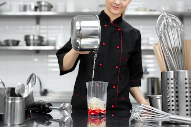 De banketbakker klopt de rode spiegelglazuur voor de cake met een blender.