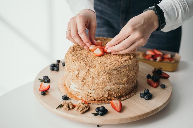 De banketbakker versiert de cake met bessen heerlijke honingcake met bessen thuis zoetwaren fabriek close-up van de hand van een banketbakker