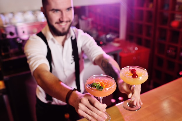 De barman die twee glazen met een oranje alcoholische cocktailglimlachen houdt