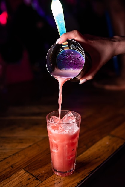 Foto de barman giet een alcoholische cocktail uit een shaker in een glas met ijs.