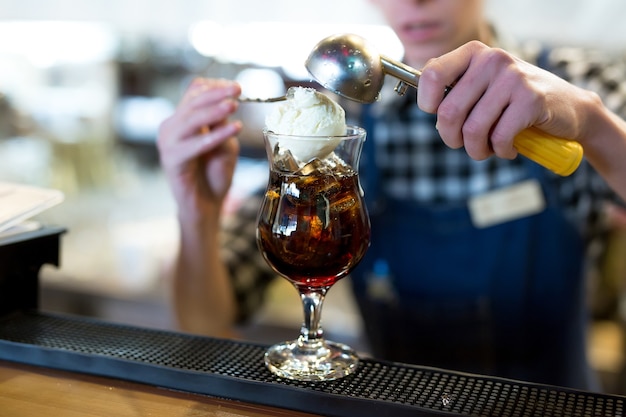 De barman in het restaurant doet een bolletje ijs in een glas met een cocktail.