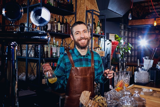 De barman lacht terwijl hij aan de bar een cocktail maakt