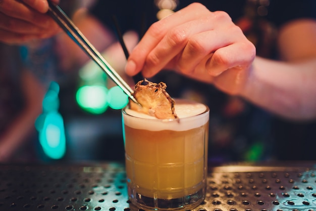 De barman maakt vlam over een cocktail met sinaasappelschil dicht omhoog.