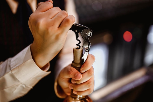 De barman opent een fles rode wijn met een wijnopener. Veel lege glazen inschenken aan de toog. Onscherpe achtergrond. wijn, proeverij, open, drank, barman, dinerconcept.