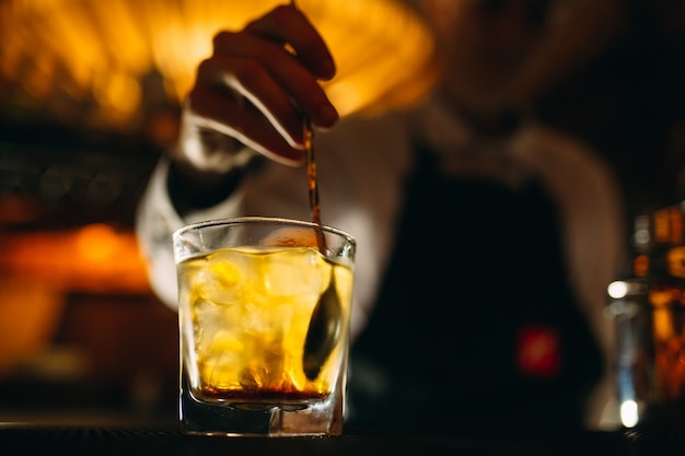 De barman roert een lepel whisky met ijs in een glas