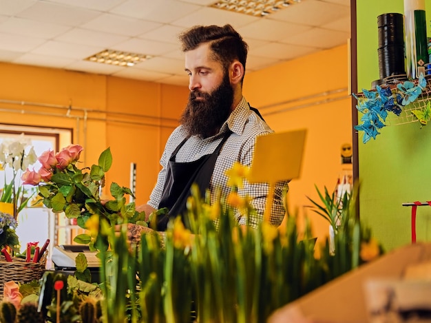 De bebaarde stijlvolle bloemenverkoper houdt roze rozen in een marktwinkel.