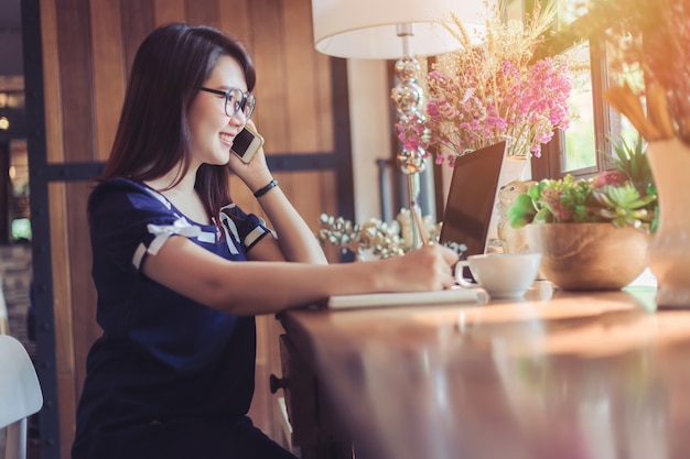 De bedrijfs vrouwengreep neemt Smartphone op werkend met laptop computer zoals in koffiewinkel