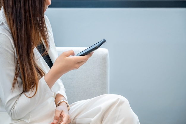 De bedrijfsvrouwen dragen witte kleren blij om mobiele telefoon op een witte achtergrond te spelen