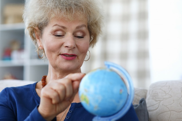 De bejaarde vrouw houdt blauwe bol in haar hand en wijst met haar wijsvinger naar continent.