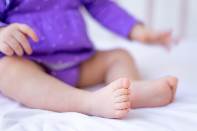 De benen of voeten van een kleine pasgeboren baby op een wit katoenen bed thuis in een wieg roze baby heels