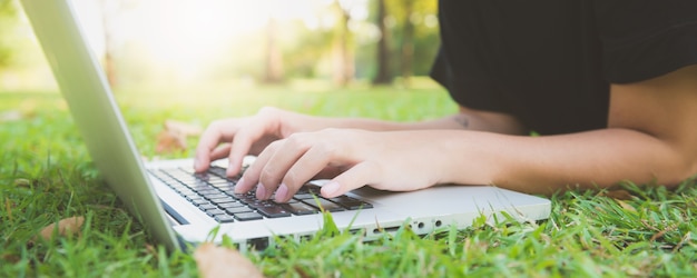 De benen van de jonge Aziatische vrouw op het groene gras met open laptop