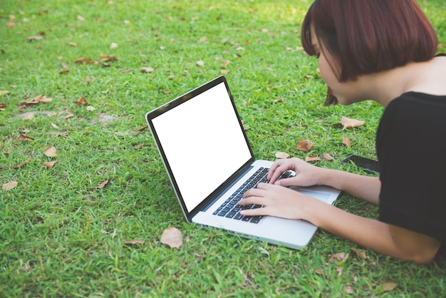 De benen van de jonge Aziatische vrouw op het groene gras met open laptop