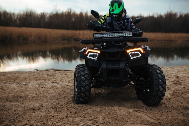 De bestuurder zit op een quad op de achtergrond de rivier en het zand. sport en extreem concept