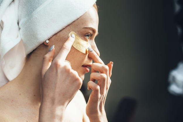 De blanke vrouw concentreert zich op het aanbrengen van hydrogel-ooglapjes onder de ogen thuis met een spa-dag