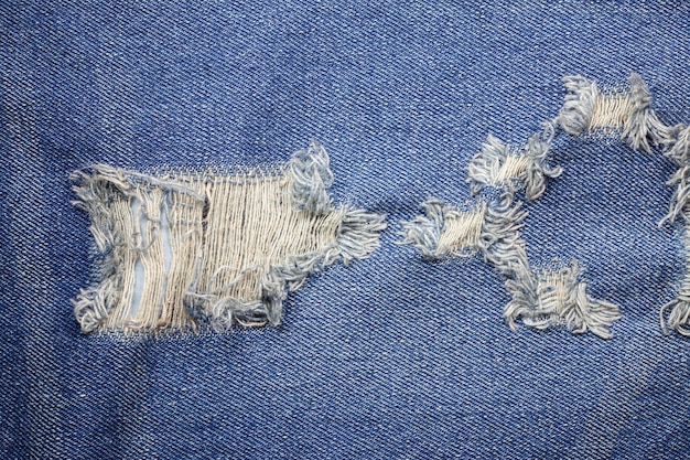 De blauwe gescheurde textuur van denimjeans.