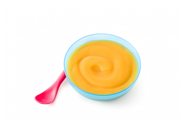 De blauwe kom van het babyvoeding met fruitpuree die op wit wordt geïsoleerd