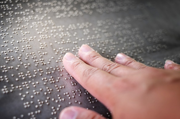 De blinde vingers raken de brailleletters op de metalen plaat