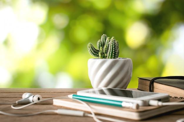 De bloemnotitieboekje, potlood en smartphone van de cactus op houten lijst met aardachtergrond.