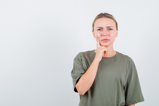 De blonde vrouw denkt door haar wijsvinger op de wang op een witte achtergrond te leggen