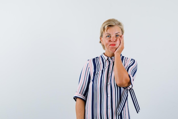 De blonde vrouw die de adem inhoudt, legt haar hand op de wang op een witte achtergrond