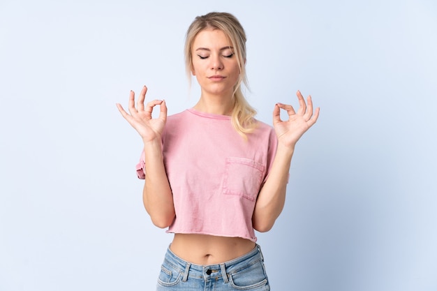 De blonde vrouw over geïsoleerde blauwe muur in zen stelt