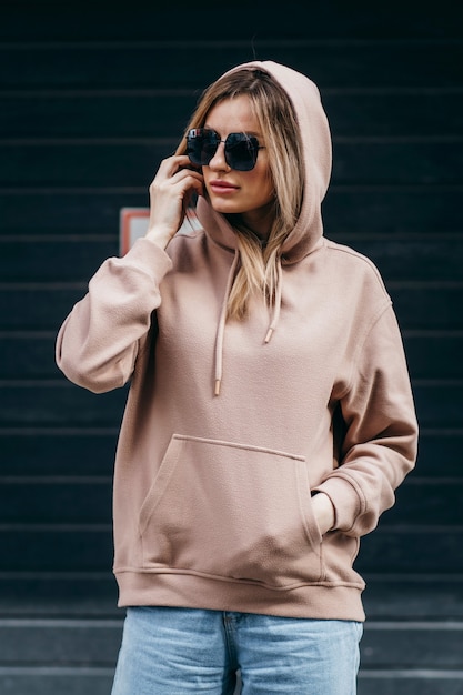 De blonde vrouw van Fasion in bruine oversized hoodieglazen en blauwe spijkerbroek