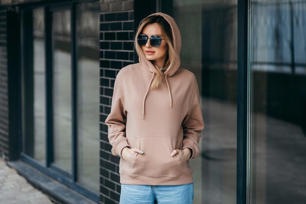 De blonde vrouw van Fasion in bruine oversized hoodieglazen en blauwe spijkerbroek