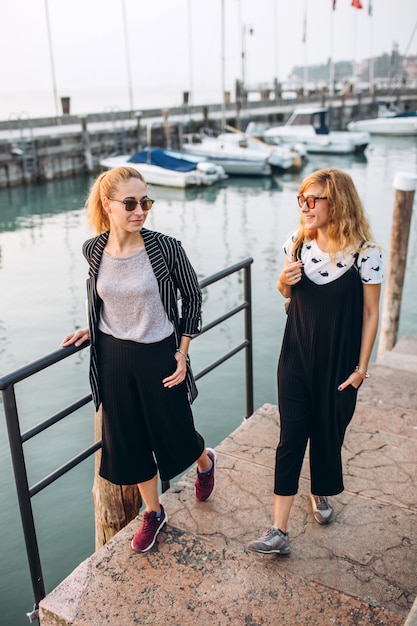 De blondemeisjes in zonnebrilmeisjes lopen langs de promenade op het Gardameer, Italië.