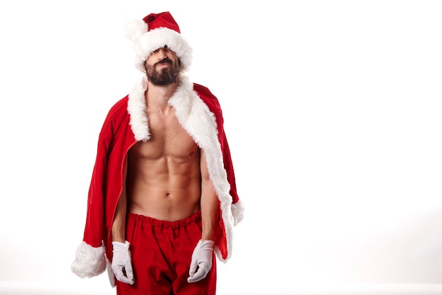 De bodybuilder van de kerstman pronkt met zijn sexy atletische lichaam op een witte achtergrond