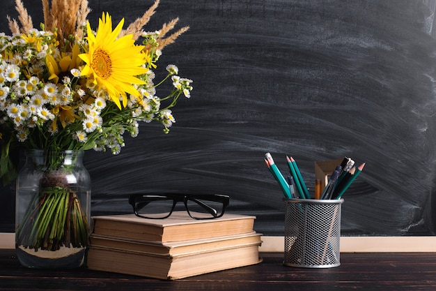 De boeken van de glazenleraar en het boeket van wilde bloemen op de lijst, op bord met krijt.