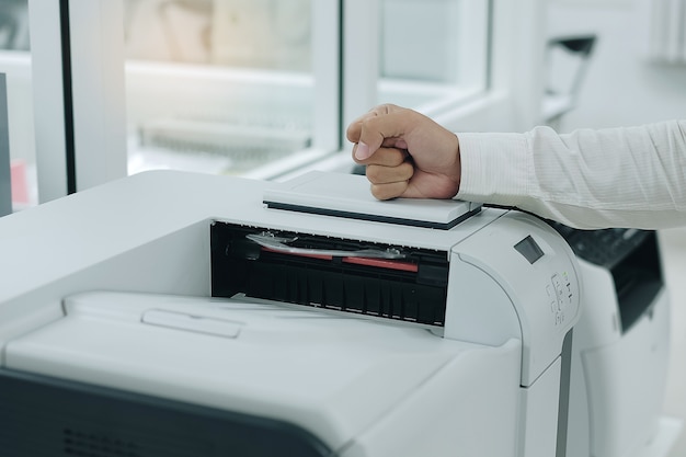 Foto de boze bedrijfsmens slaat zijn vuist op printerscanner of laserkopieerapparaatmachine in bureau
