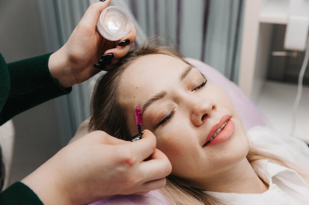 De browist kamt de wenkbrauwen met een borstel wenkbrauw verzorging in de salon