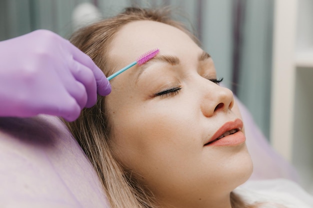 De browist kamt de wenkbrauwen met een borstel wenkbrauw verzorging in de salon