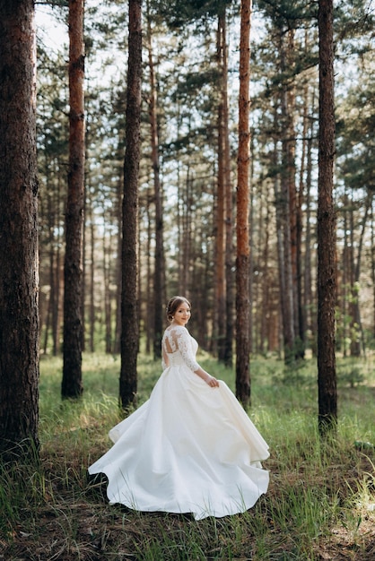 De bruid die op een heldere dag in een dennenbos loopt