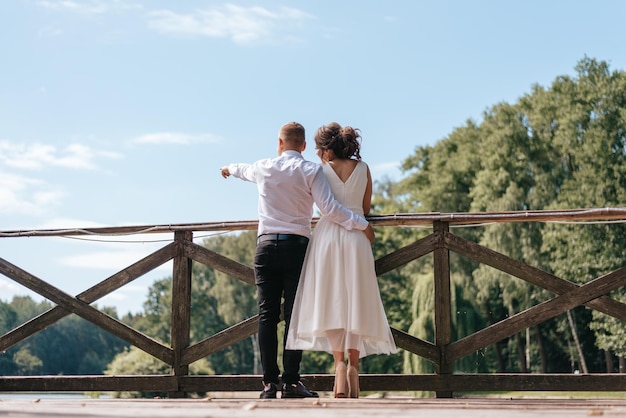 De bruid en bruidegom die elkaar omhelzen staan op de pier van een meertje en kijken in de verte