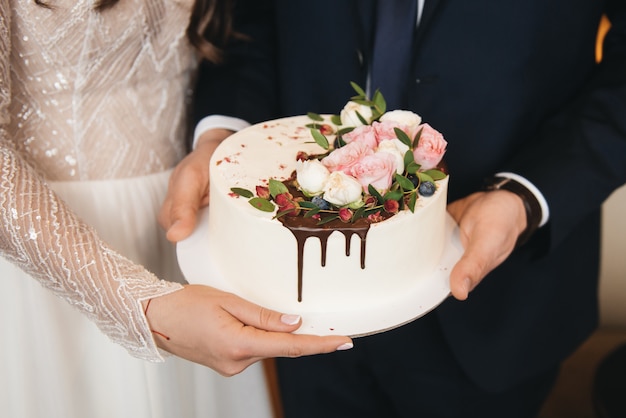 De bruid en bruidegom houden een kleine bruidstaart versierd met chocolade en bloemen