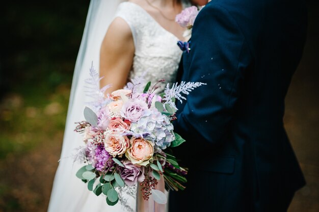 De bruid en bruidegom met een bruiloft boeket, hand in hand en staande op de huwelijksceremonie van de buitenlucht in de achtertuin van de natuur.