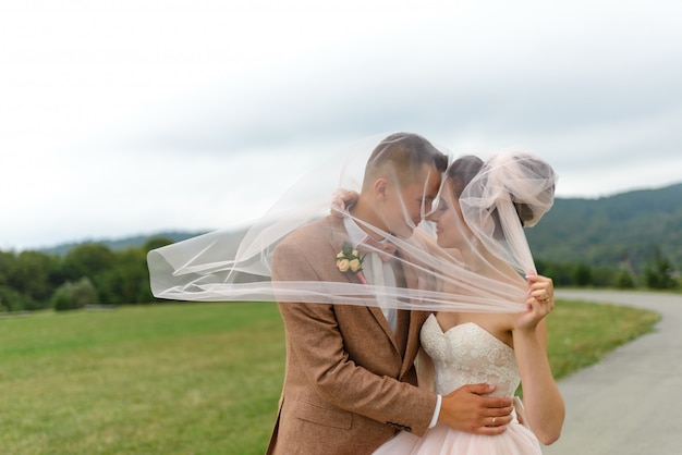 De bruid en bruidegom omhelzen elkaar onder een sluier en buigen zachtjes hun hoofd naar elkaar.
